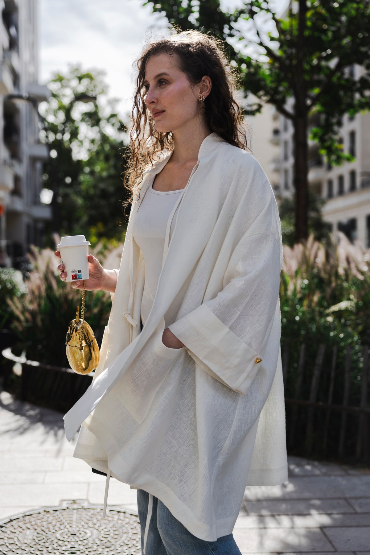 Side view of the MAATHI Souffle white linen coat beside a garden railing.