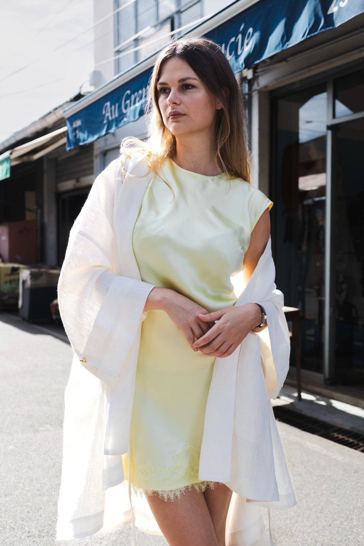 MAATHI white linen coat styled with a pale yellow dress beside market stalls.