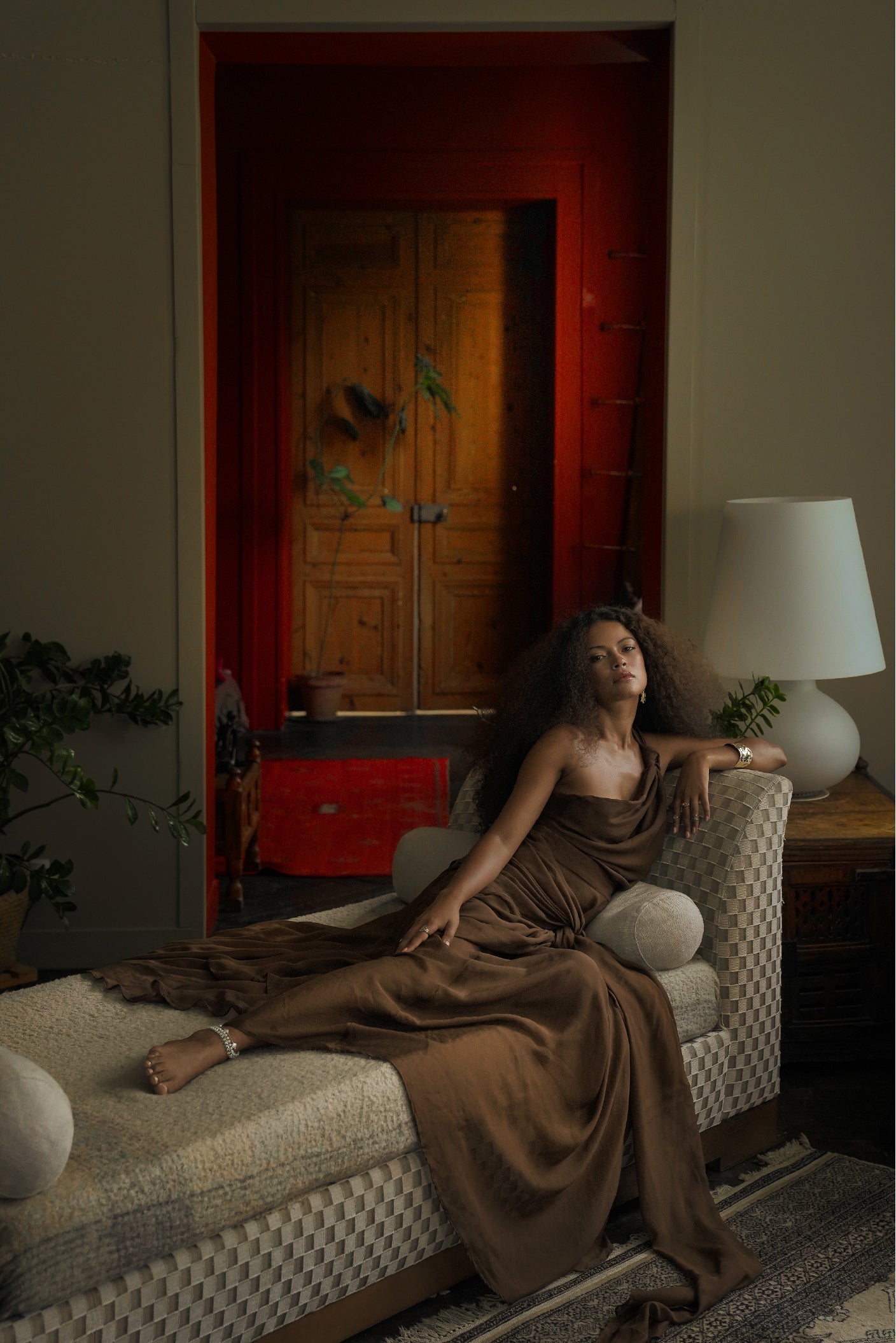 Model reclining indoors wearing the Drift Silk Skirt and Ebb Silk Knot Top in flowing brown silk with elegant draped styling