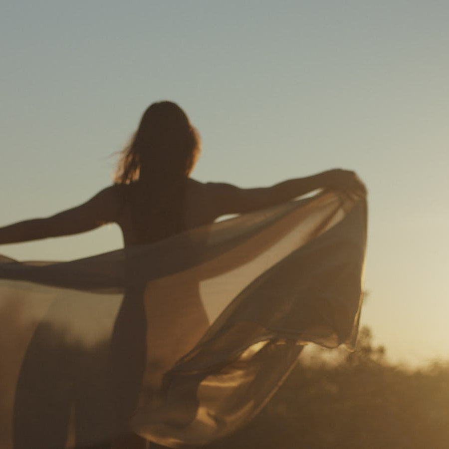 Woman silhouetted at sunset holding a flowing Maathi silk fabric, embodying slow luxury, movement, and sustainable craftsmanship.