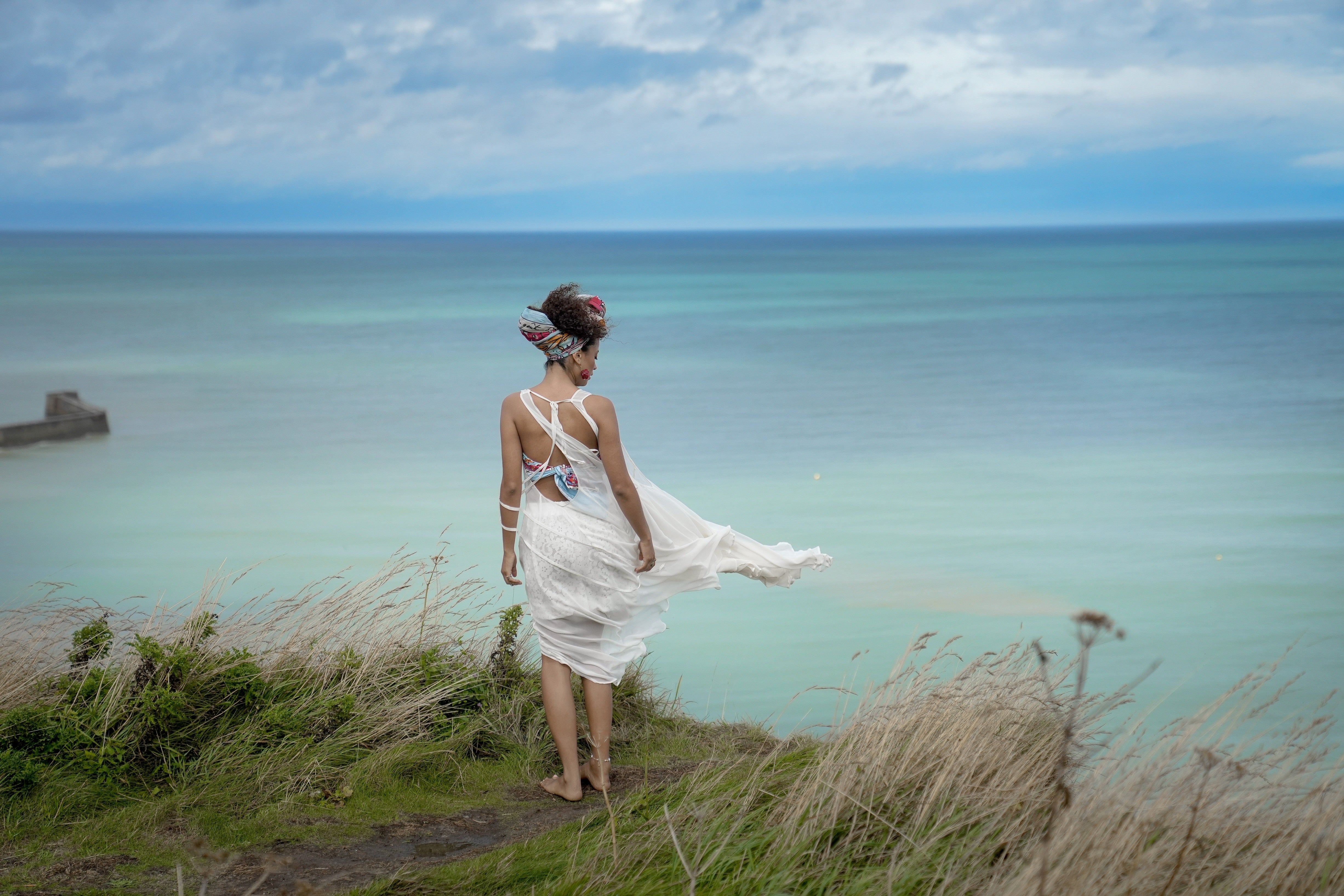 A woman in flowing white by the sea, expressing modern luxury through time, space, and escape.