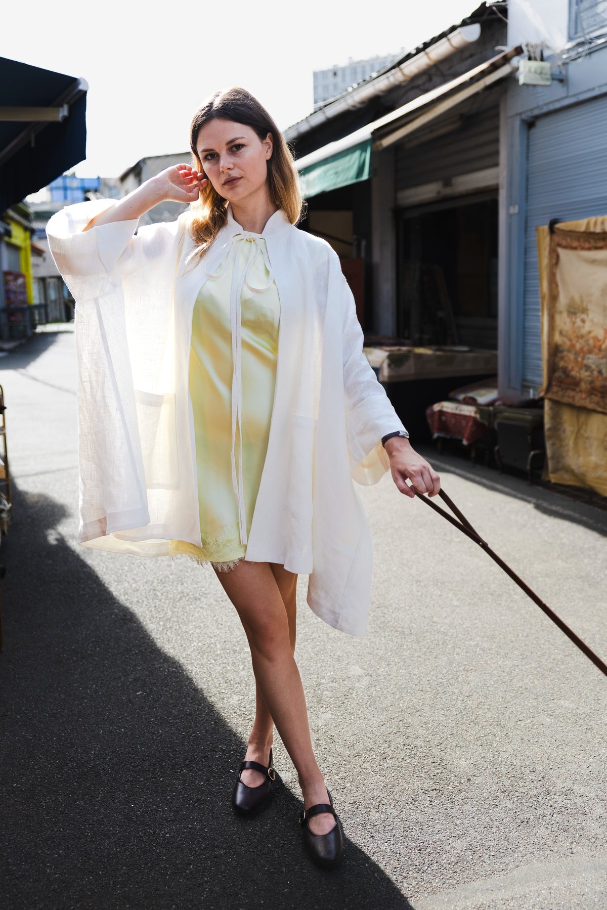 MAATHI white linen coat worn over a pale yellow dress on a market street.